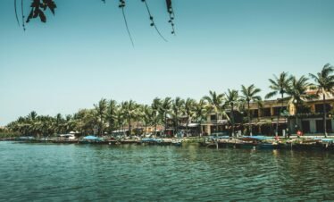 A serene riverside scene with palm trees and traditional Vietnamese houses, perfect for travel imagery.